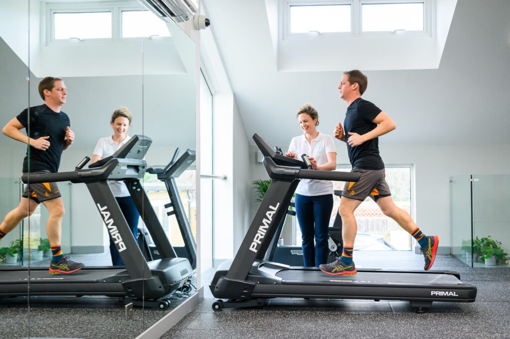 Physiotherapist standing next to man running on treadmill.