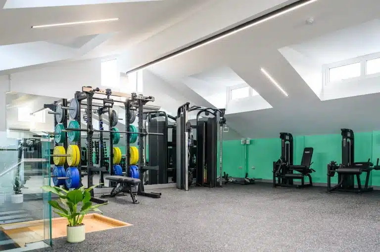 Photo of a bright, modern gym with weightlifting racks, barbells, and strength training equipment