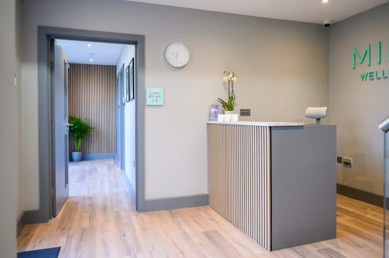 Photo of the Mint Wellbeing clinic reception with a desk, orchid, and hallway to treatment rooms