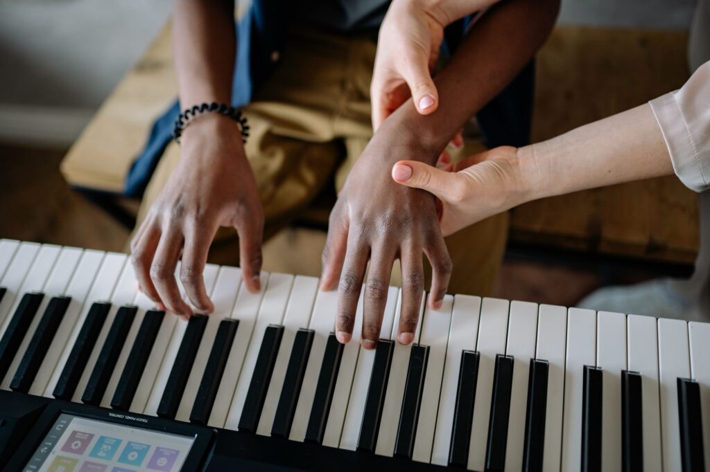 Photo of a person guiding a pianist's wrist and fingers on a keyboard