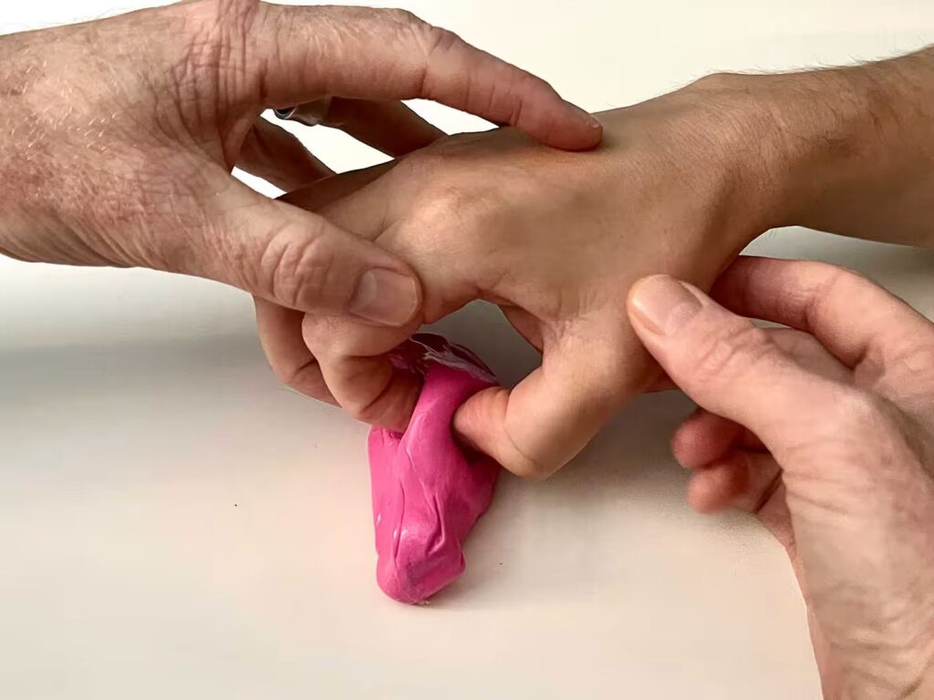 Photo of a hand therapist steadying a patient's hand as they press a finger into therapy putty